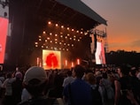 Outdoor concert stage with vibrant lighting and enthusiastic crowd at sunset