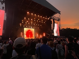 Outdoor concert stage with vibrant lighting and enthusiastic crowd at sunset