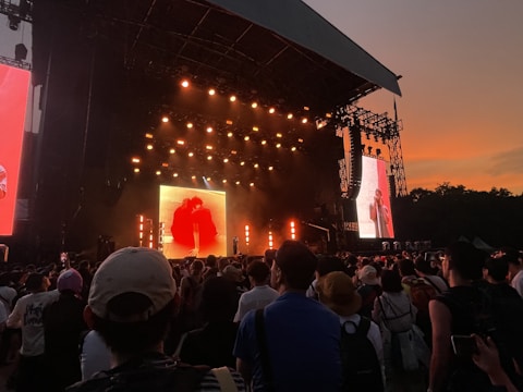 Outdoor concert stage with vibrant lighting and enthusiastic crowd at sunset