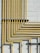 A series of yellow pipes run vertically and horizontally against a light gray concrete block wall, creating a grid-like pattern. The pipes are evenly spaced and neatly arranged, showcasing a structured and industrial design.