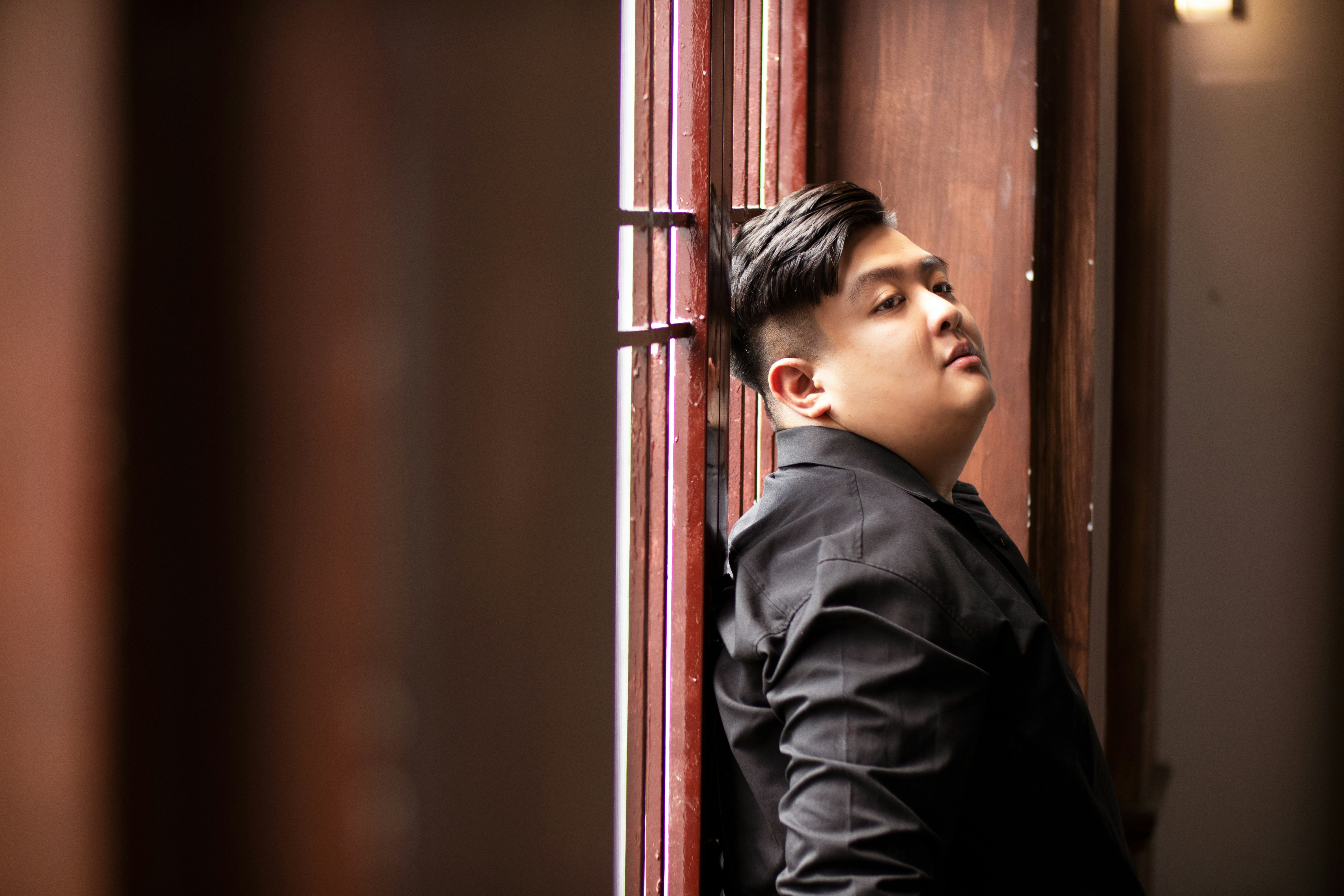 a young man leaning against a wooden wall