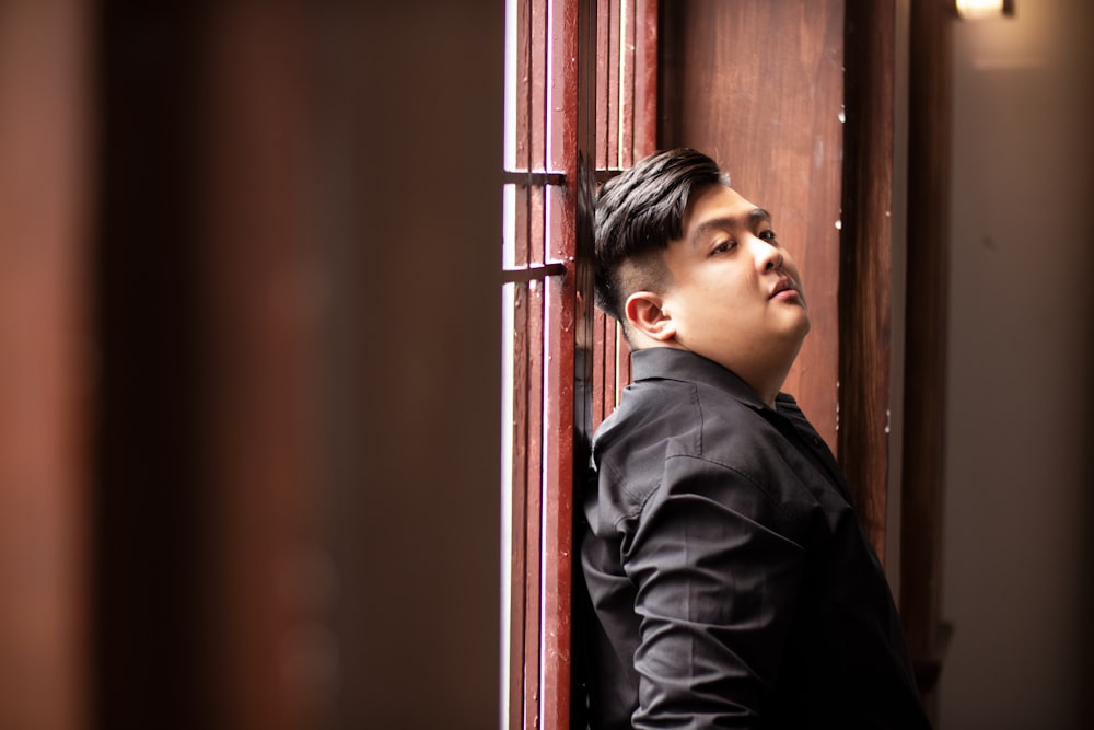 a young man leaning against a wooden wall