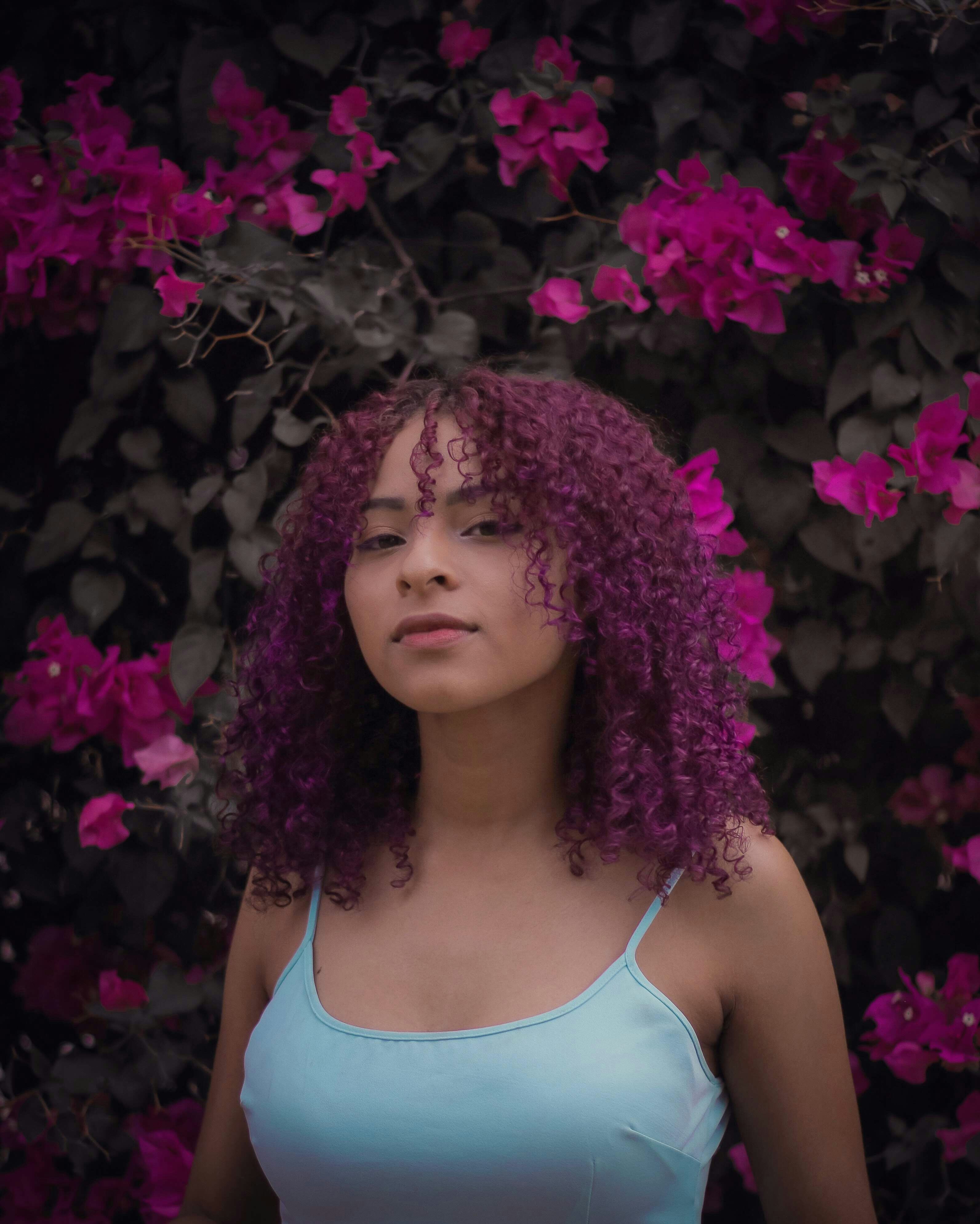 a woman with purple hair standing in front of a bush