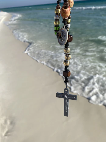 Faith-inspired beach jewelry displayed on driftwood with ocean waves in the background.