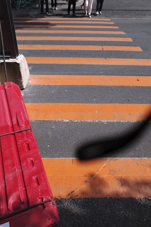 Pedestrian ADA-compliant barricades lined up along a sidewalk, painted in stark white and safety orange for maximum visibility.