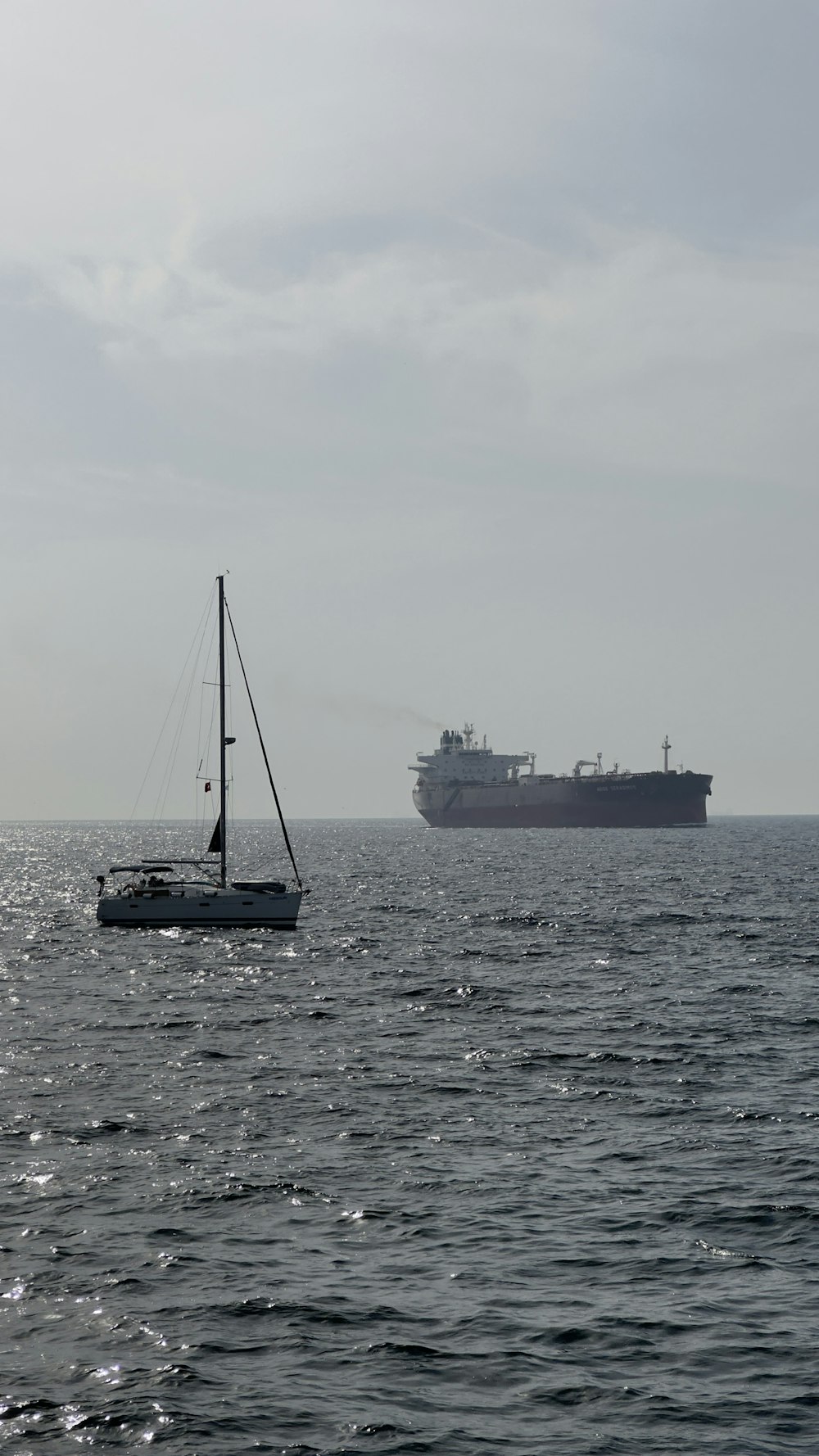 a sailboat in the ocean with a large ship in the background