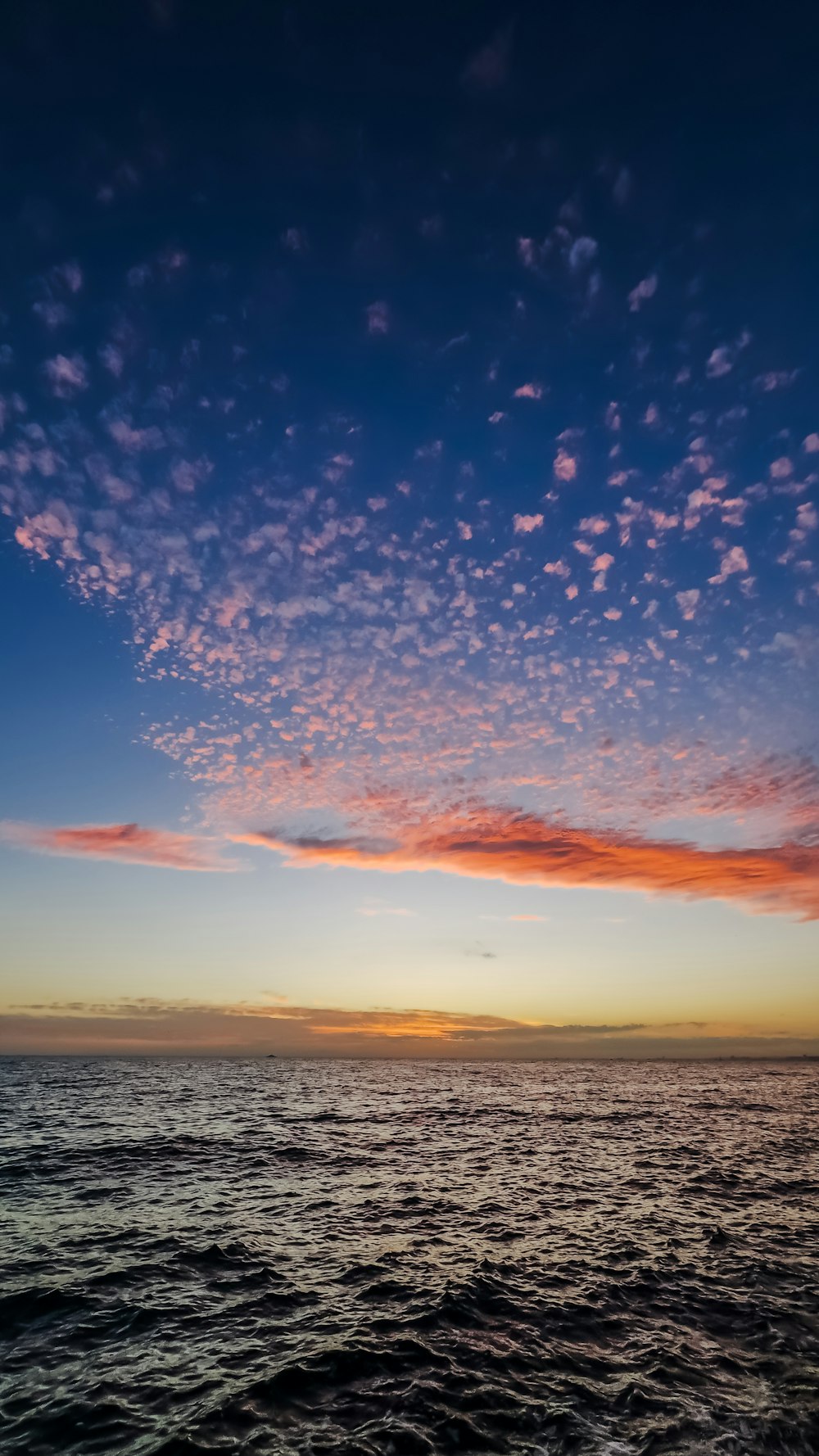 the sun is setting over the ocean with clouds in the sky