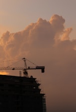 A powerful crane lifting steel beams high above a bustling construction site at sunrise.