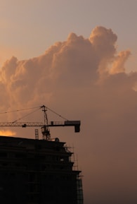 A rugged yellow crane lifting steel beams at a busy construction site during sunrise.
