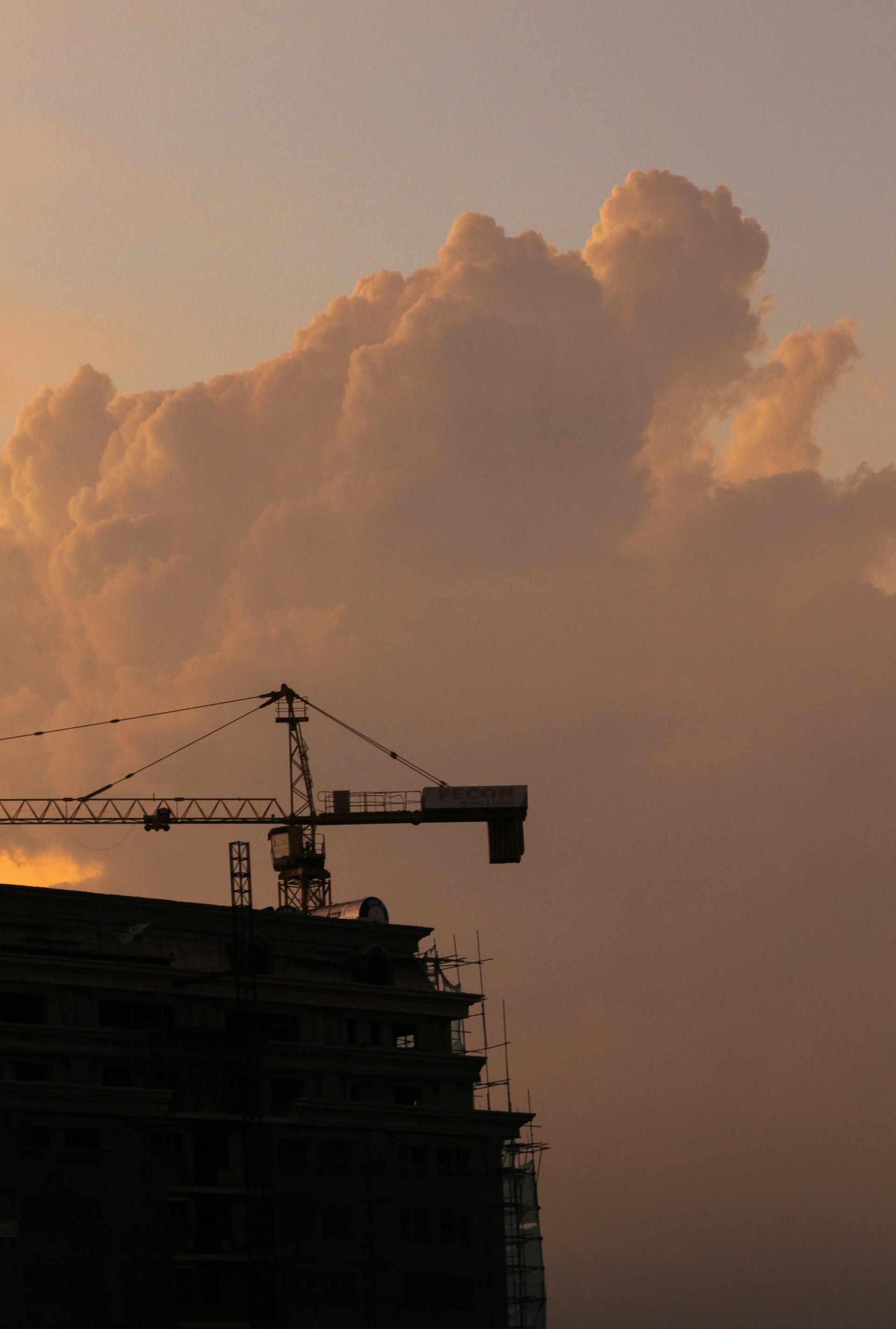 A powerful crane lifting heavy steel beams at a construction site during sunset.