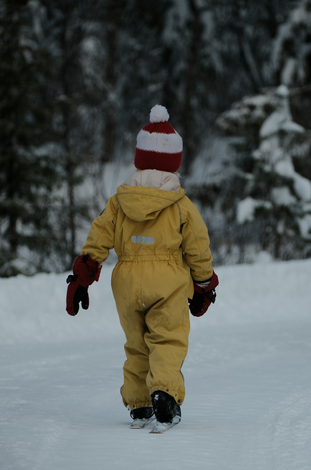 a small child in a yellow snowsuit walking in the snow