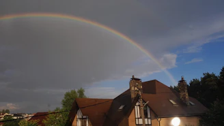 A bright and cheerful painting of a rainbow arching over a cozy house.
