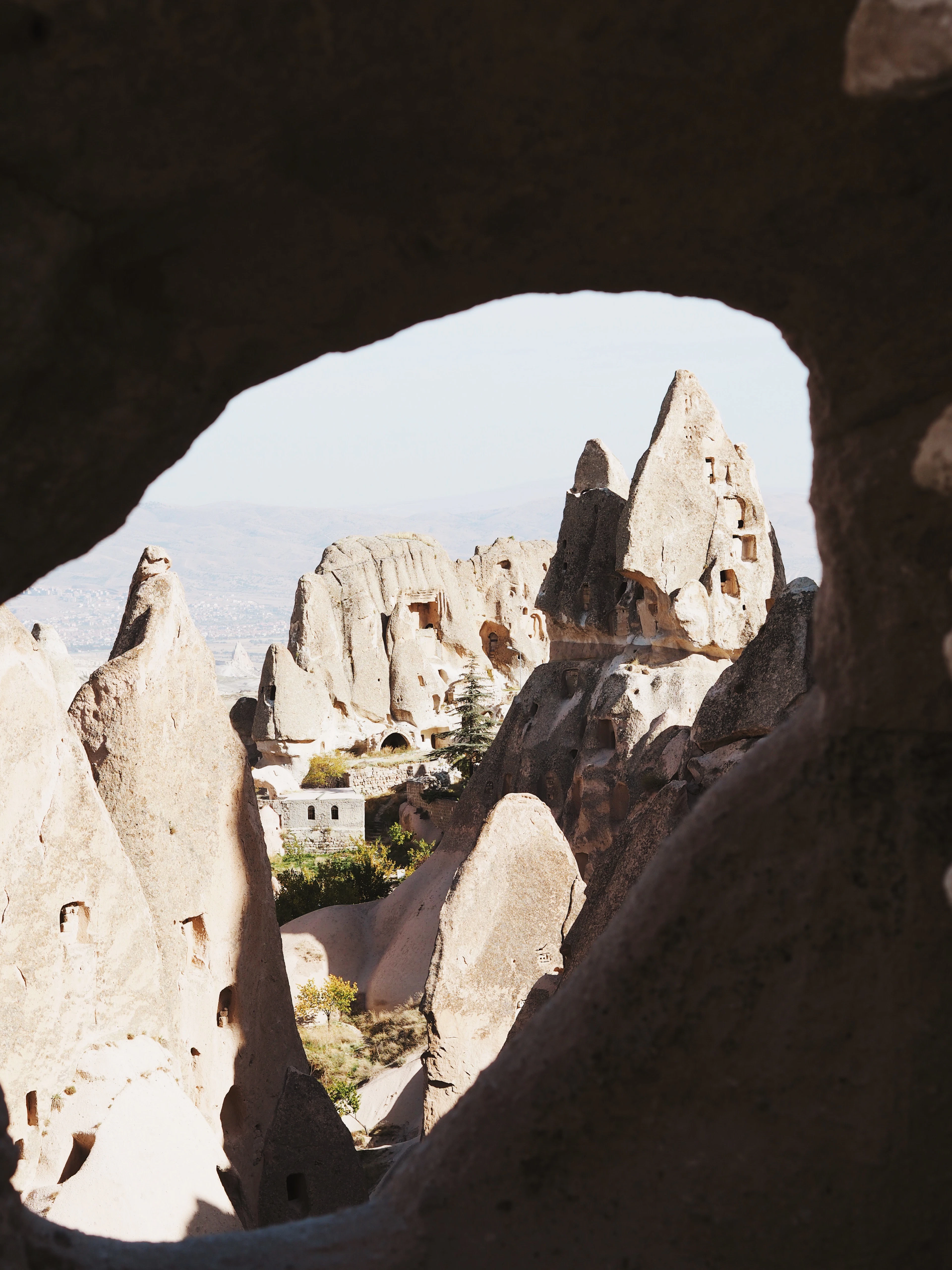 A rock-cut cave opening frames a distant view of Cappadocia's fairy chimneys and cave dwellings.