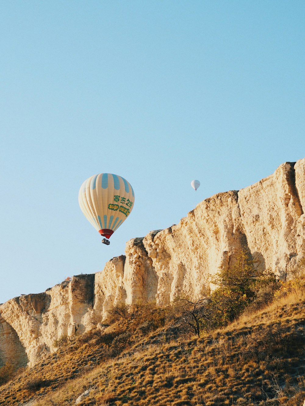 two hot air balloons flying over a rocky hillside