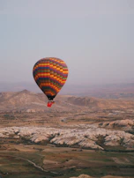 A colorful hot air balloon floating peacefully over rolling countryside at dawn.