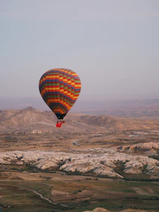 A colorful hot air balloon soaring over lush green landscapes at sunrise.