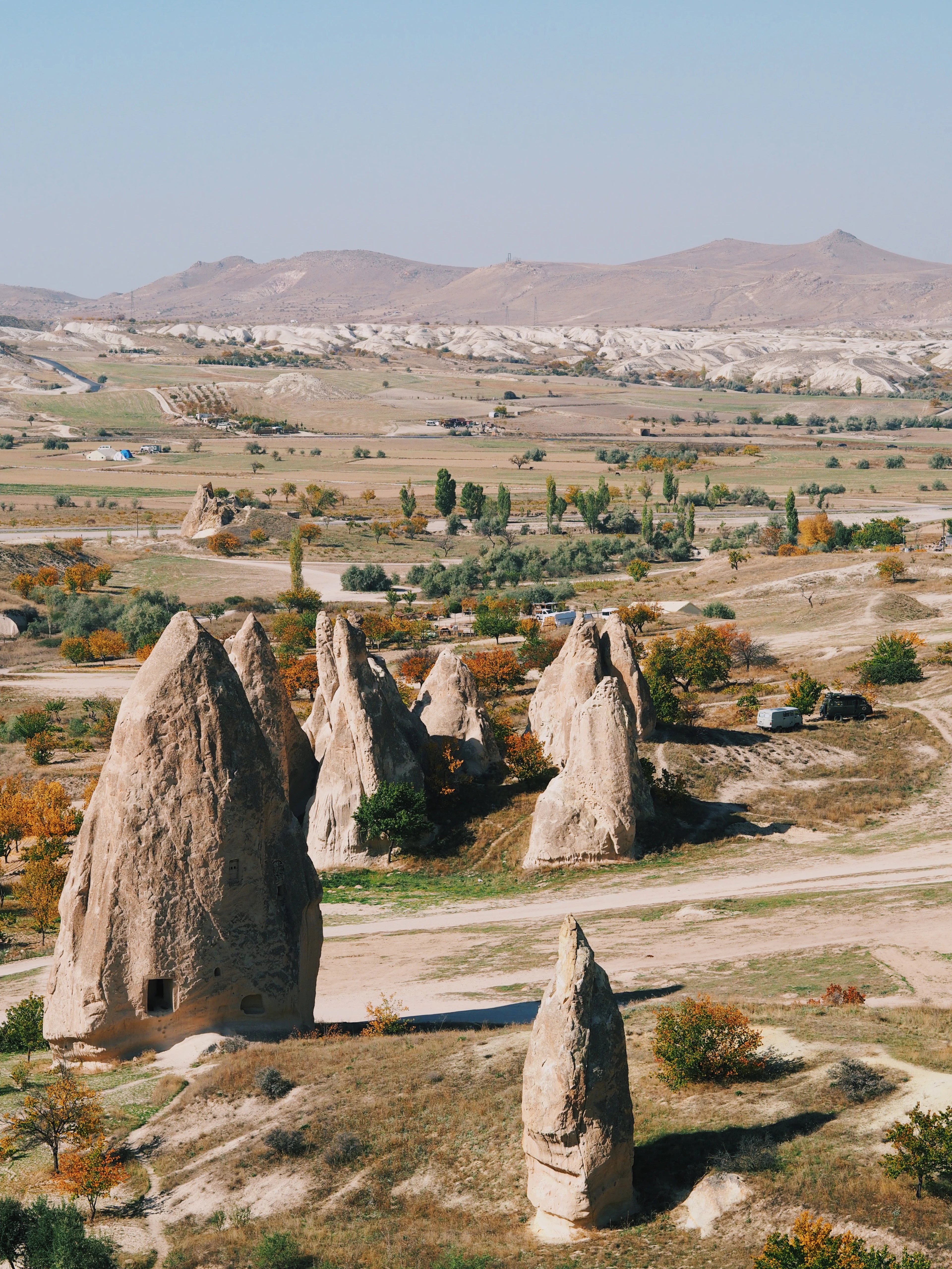 Red Valley fairy chimneys rising from autumn-orange foliage with farmland in the distance.