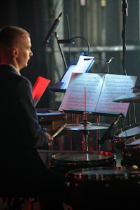 Drummer reading rhythmic notation while practicing on a drum set.