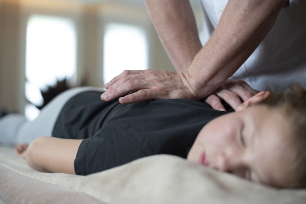 A person is lying face down on a comfortable surface, receiving a massage from another individual's hands. The setting appears calm and serene, with soft lighting enhancing the relaxed atmosphere. The person receiving the massage has closed eyes, indicating a state of relaxation.