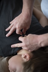 A person wearing a dark shirt is lying down, while another person's hands are pressing on their back or chest area. This seems to be either a massage or a therapy session.