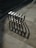 Metallic geometric structure resembling a bike rack is casting intricate shadows on the stone pavement, with the shadows extending in patterns due to the sunlight. The pavement is made up of square tiles of varying shades.