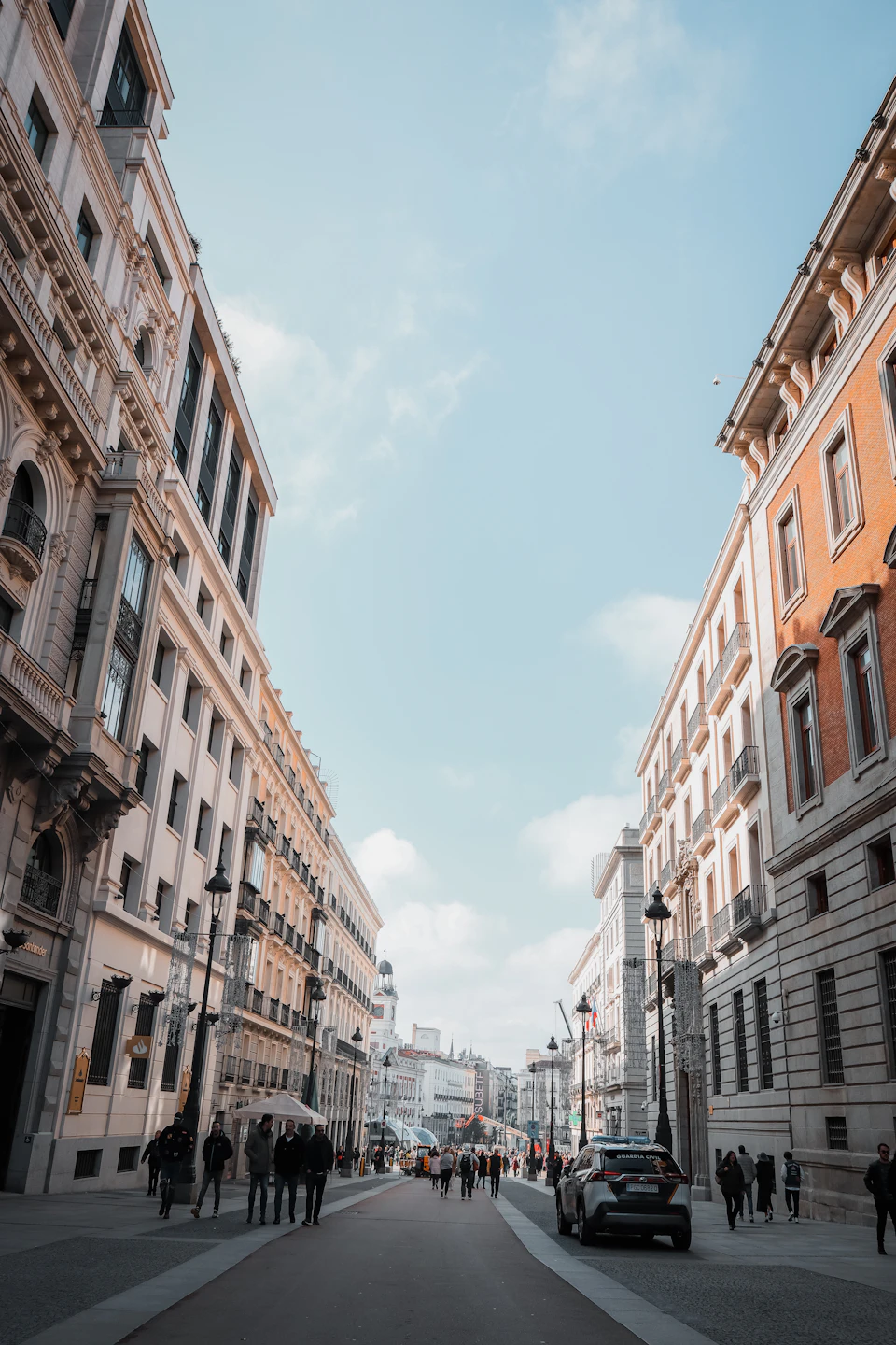 Bustling city street with tall buildings lining both sides from ground level perspective