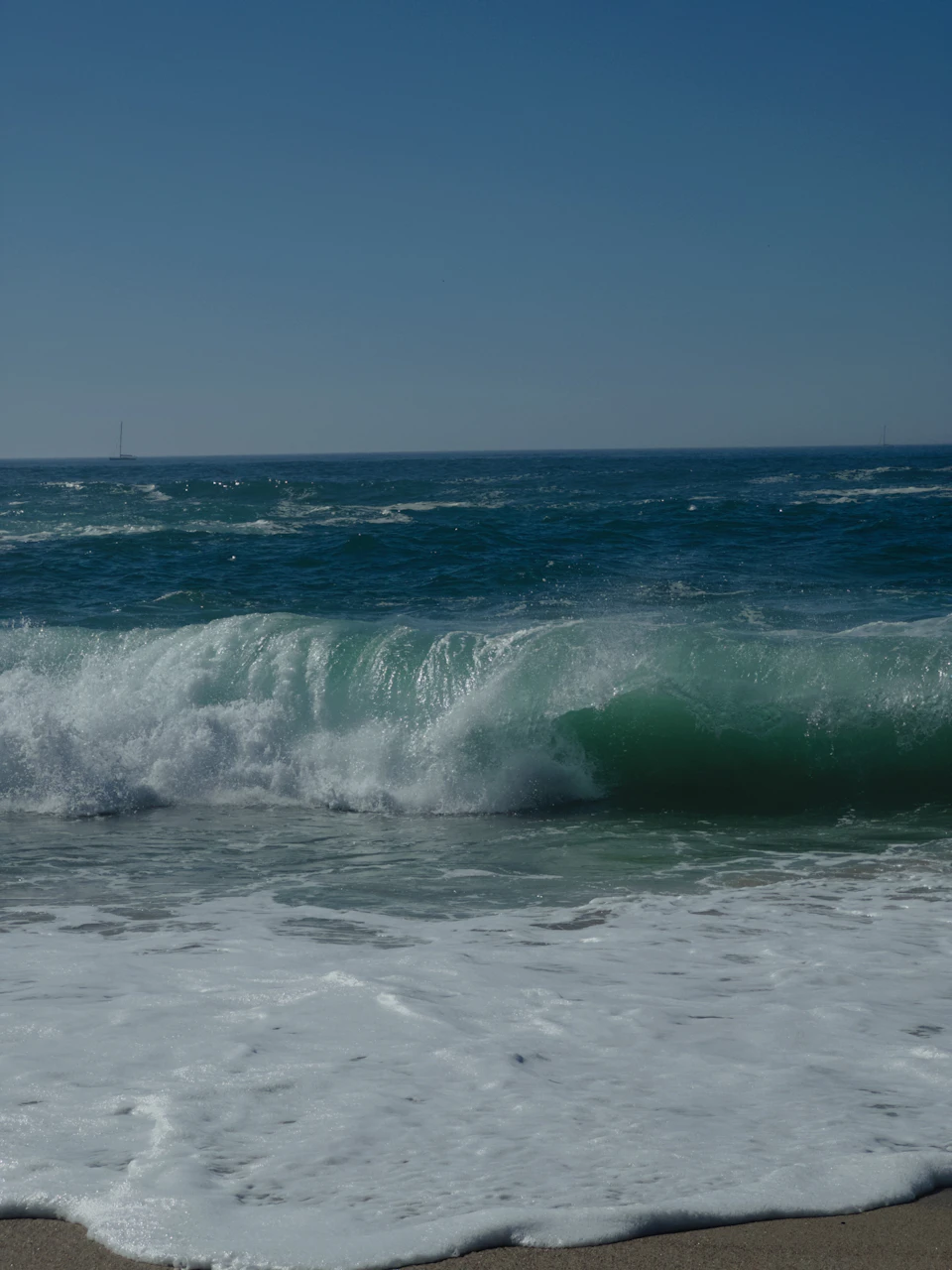 Large wave crashes onto the shore in a serene beach scene with calm waters