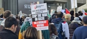 A crowd of people participating in a protest, holding various signs that express opposition to the war in Gaza. The central sign calls for a socialist intifada, organized by the Socialist Party. Many participants are wearing jackets and backpacks.
