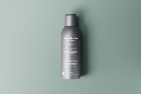 A minimalistic mockup of a large spray can, positioned against a smooth, muted green background. The can is a sleek gray with white text providing details about its features and instructions. Its shadow subtly appears on the surface, indicating soft lighting.