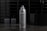 A sleek, silver spray can is prominently displayed on a reflective surface. The background features a black glossy tiled wall and blurred shapes that resemble containers, adding to the minimalist aesthetic.