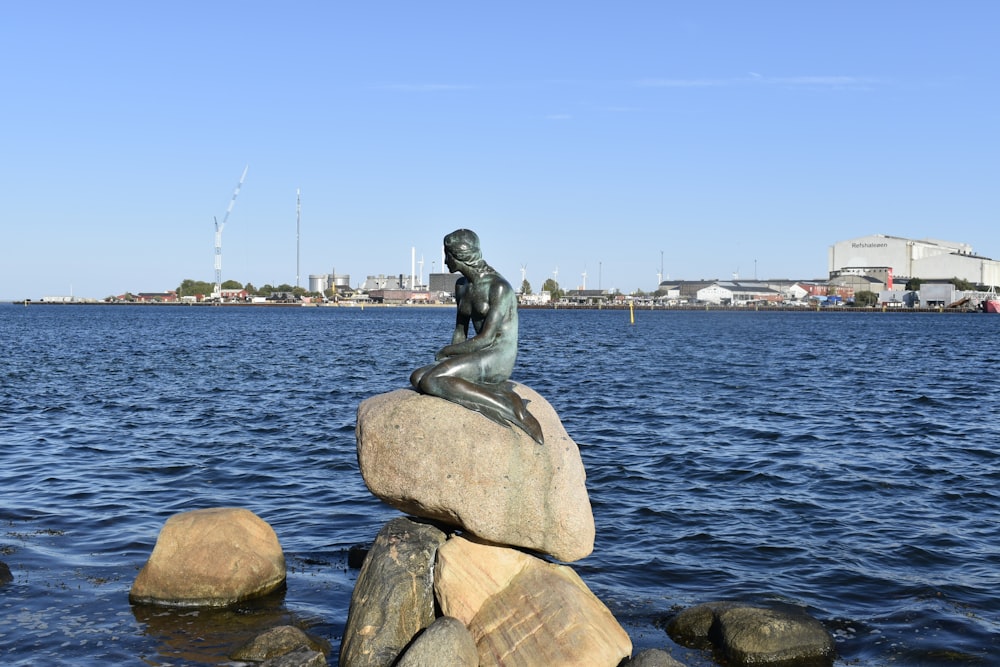 uma estátua de uma sereia sentada no topo de uma rocha