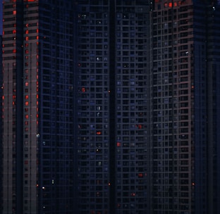 A fortified apartment complex with red neon accents and surveillance cameras glaring in the night.