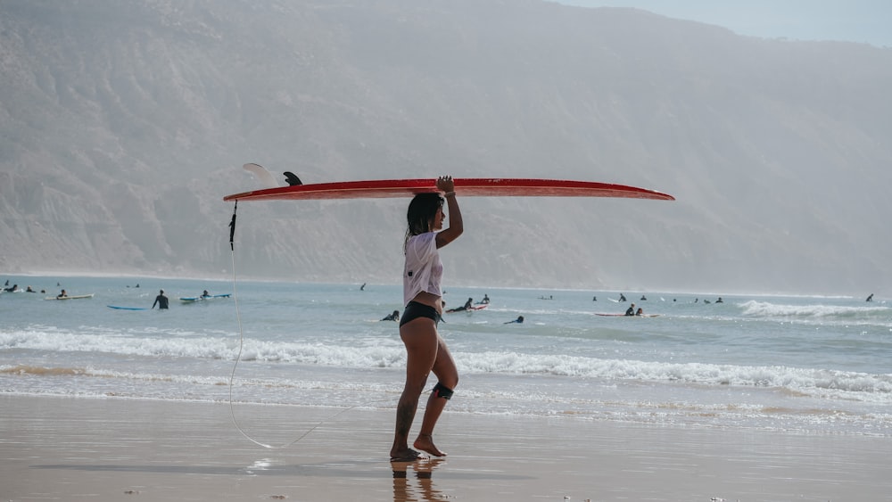 a woman holding a surfboard on top of a sandy beach