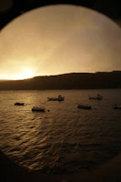 Sunset over a serene bay with traditional fishing boats gently floating on calm waters.