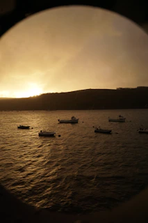 A peaceful sunset over a protected bay, where fishing boats rest along the horizon.
