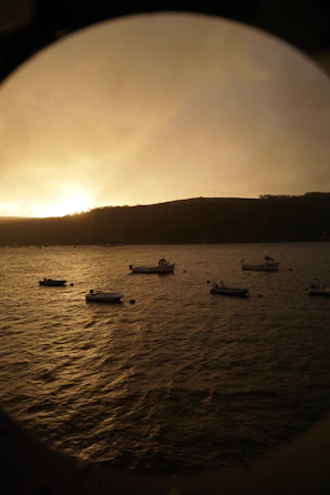 Sunset over a serene bay with traditional fishing boats gently floating on calm waters.
