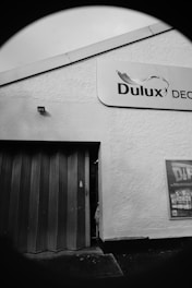 A building facade with a Dulux sign is visible, featuring a partial open wooden door and an advertisement poster on the textured wall.