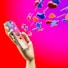 A wooden mannequin hand holding a smartphone, with heart and like icons emerging from the screen against a bright pink and red background. The icons appear three-dimensional and colorful, symbolizing social media engagement.
