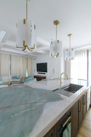 A modern kitchen area with sleek white countertops and golden fixtures.