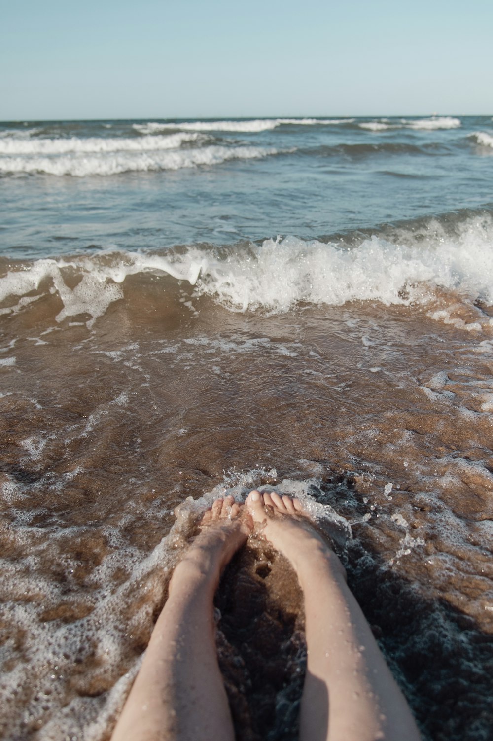 a person laying on the beach with their feet in the water