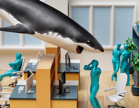 In an office setting, a large shark floats above workstations, surrounded by blue humanoid figures. One figure appears to be startled with hands on their head, while others stand nearby. The office has light wood flooring, yellow partitions, white chairs, and computer desks. Plants are visible in the background.