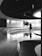 A modern, circular interior space features reflective flooring and a smooth, curved wall structure. Natural light pours in from large windows, illuminating a solitary tree in the background. A blurred silhouette of a person walks through the scene, adding a sense of movement.