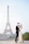 Couple taking photos in front of the Eiffel Tower on a bright day.