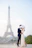 Couple taking photos in front of the Eiffel Tower on a bright day.