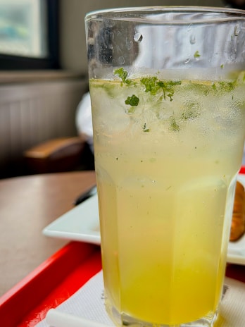 A refreshing glass of homemade lemonade with mint leaves and ice, glowing in natural light.