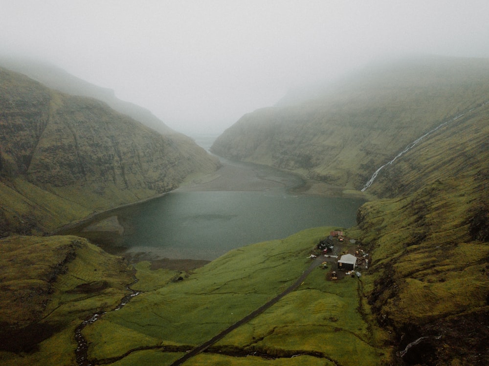 a lake surrounded by green hills and fog