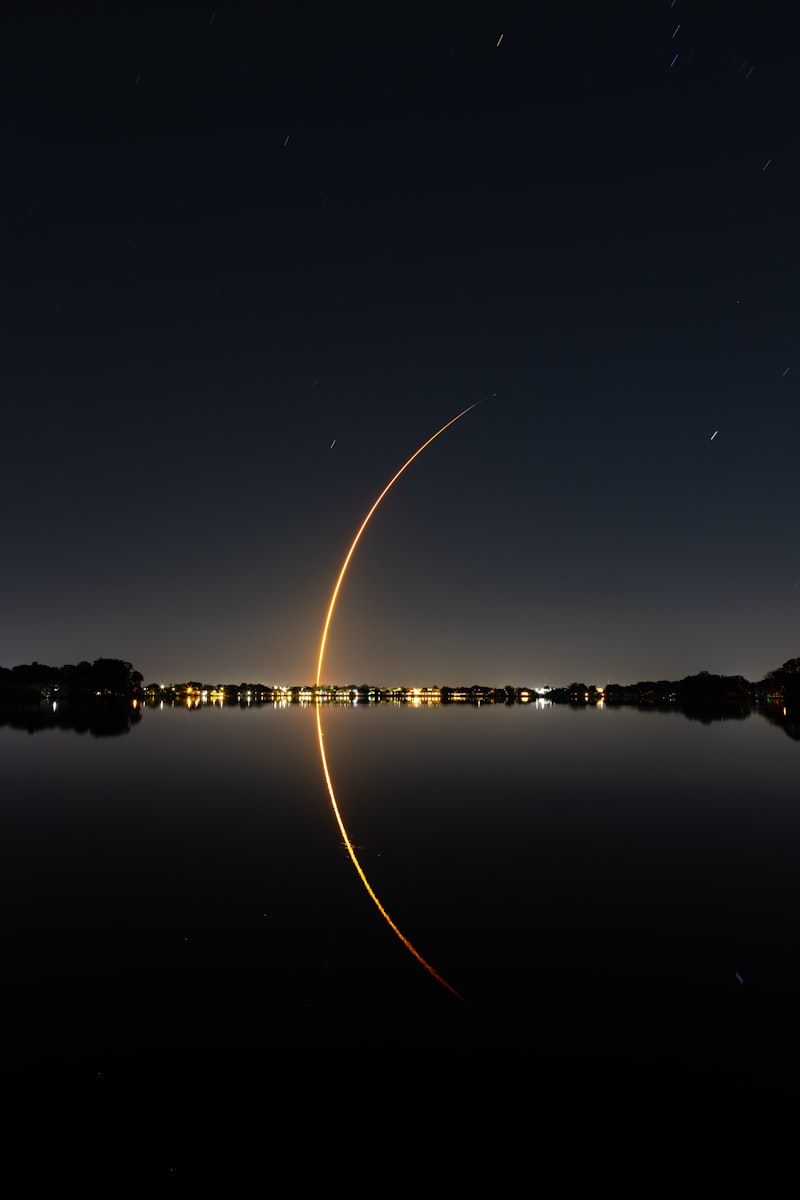 Long-exposure photograph of a rocket launch arc reflected in water at night