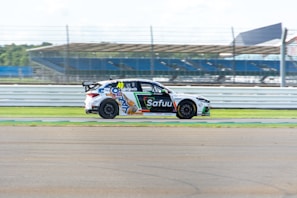 Dynamic shot of the race car speeding on the track with sponsor banners in the background.