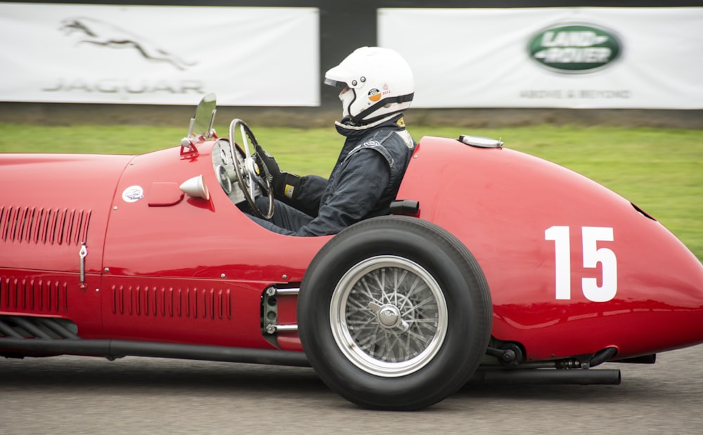 a man driving a red race car down a street