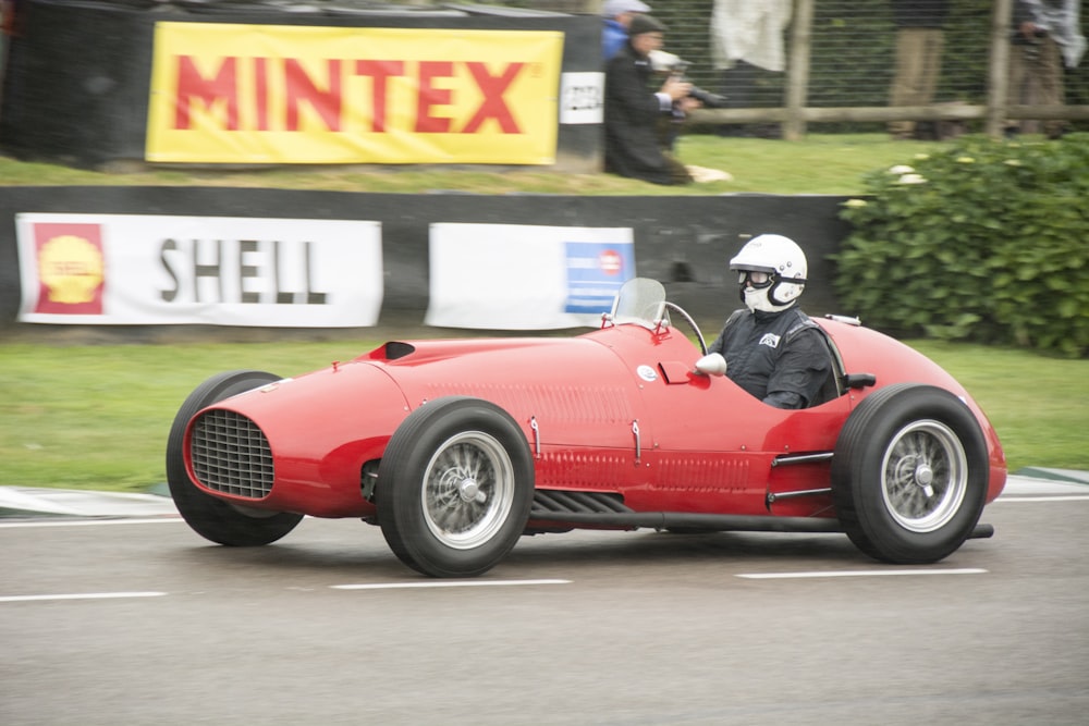 a man driving a red race car down a street